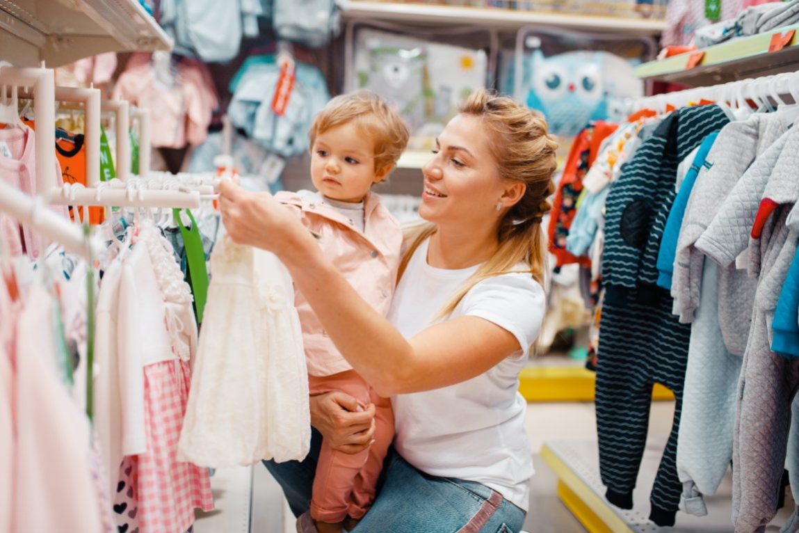Mother with girl choosing clothes in kids store