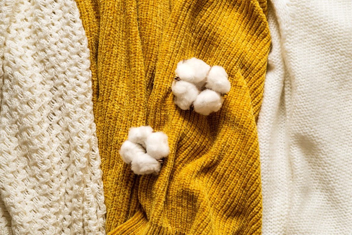 Fall Background with warm sweaters. Pile of knitted clothes with autumn leaves, warm background, knitwear, space for text