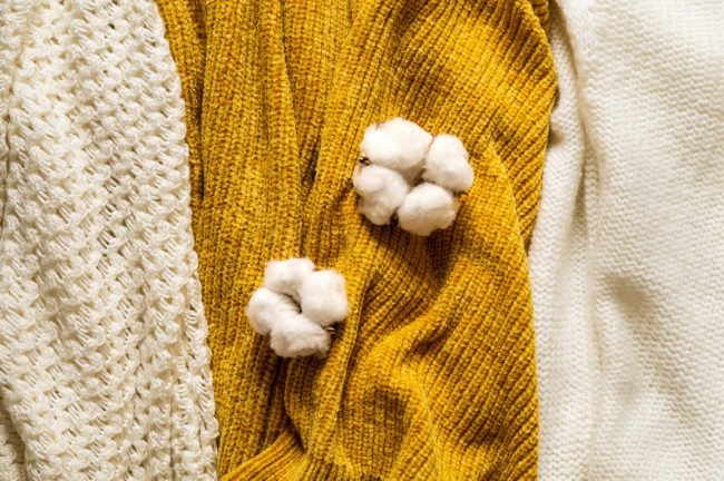 Fall Background with warm sweaters. Pile of knitted clothes with autumn leaves, warm background, knitwear, space for text