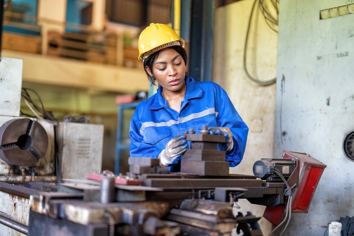 Woman worker in uniform operating machine at factory concentrate on fabrication job on lathe