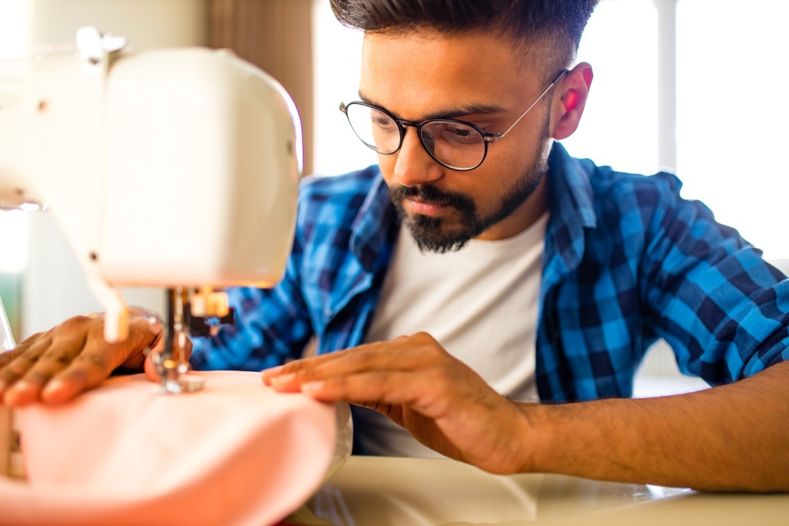 arabian man designer sewing clothes on sewing machine in studio workplace home