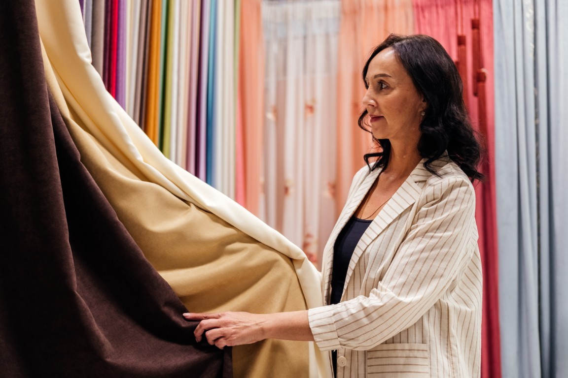 Mature woman choosing curtains in textile store indoor. Designer working and combining colors and textures