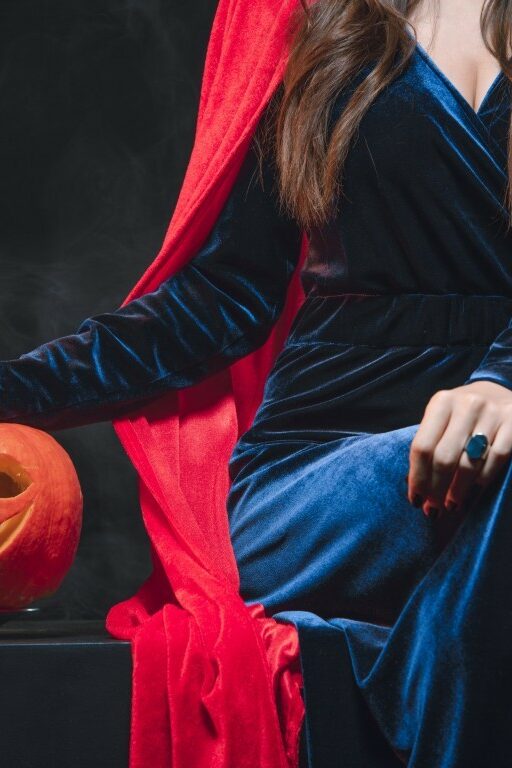 cropped view of woman in red cloak with jack o lantern on darkness with smoke