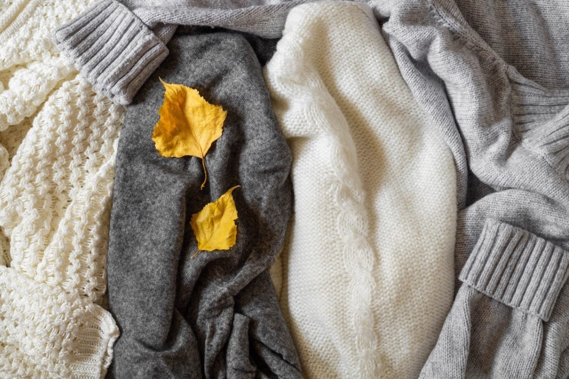 Pile of knitted clothes with autumn leaves, warm background, knitwear, space for text