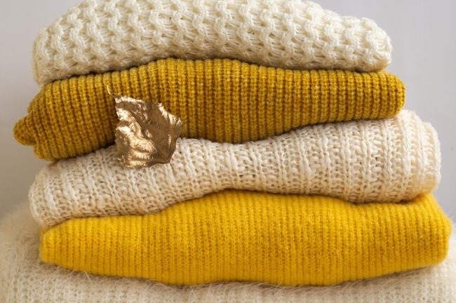Autumn winter concept. Pile of knitted clothes with autumn gold leaves, warm background, knitwear