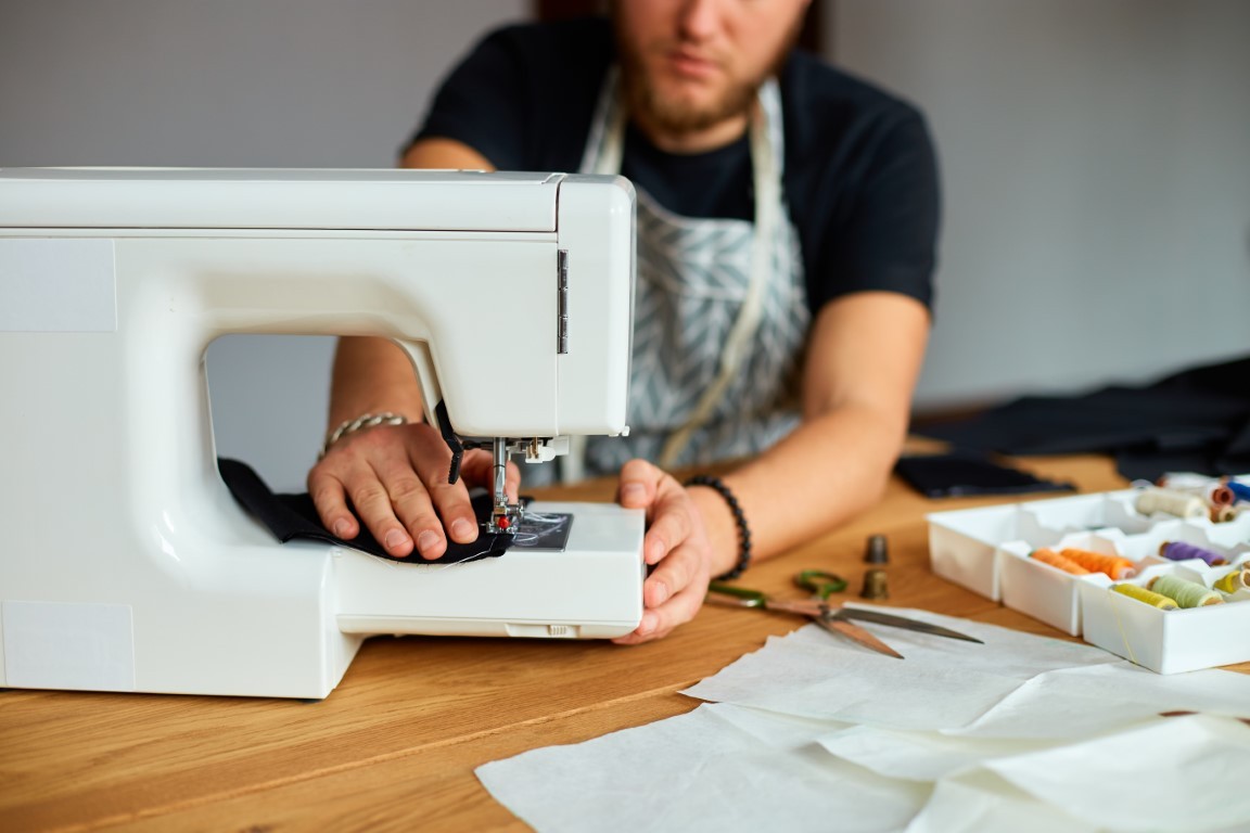 Man sews clothes on sewing machine,  male tailor working with sewing in atelier